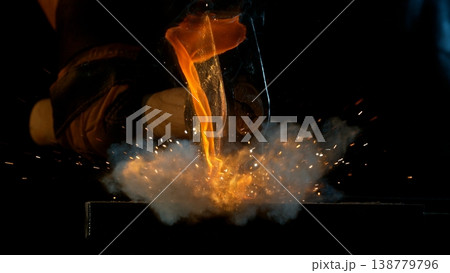 Close-up of blacksmith forging glowing hot iron on anvil with flying sparks 138779796