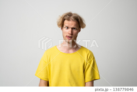 Young blonde man making a silly face, crossing one eye and sticking out his tongue, expressing a playful and foolish mood on a neutral background Young blonde man making a silly face, crossing one eye and sticking out his tongue, expressing a playful and foolish mood on a neutral background 138779846