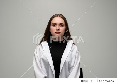 Young woman posing in a studio for a headshot, wearing a white shirt over a black top with long brown hair Young woman posing in a studio for a headshot, wearing a white shirt over a black top with long brown hair 138779873