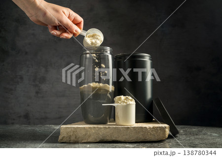 Vanilla whey protein powder and shaker, food supplements, dark background. Making protein shake drink. Vanilla whey protein powder and shaker, food supplements, dark background. Making protein shake drink. 138780344
