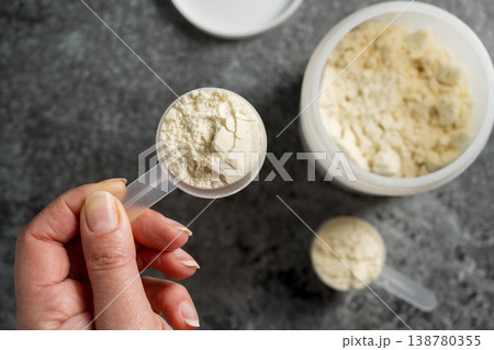 Female hands holding a scoop of protein whey powder, white plastic tube, on dark background Female hands holding a scoop of protein whey powder, white plastic tube, on dark background 138780355