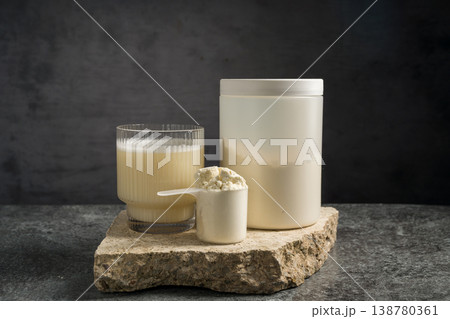 Protein vanilla shake in drinking glass, scoop with whey protein powder and white plastic tube, on dark background Protein vanilla shake in drinking glass, scoop with whey protein powder and white plastic tube, on dark background 138780361