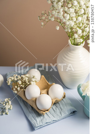 Easter eggs background. White eggs in cardboard box and gypsophila flowers in a vase. Spring holiday Easter eggs background. White eggs in cardboard box and gypsophila flowers in a vase. Spring holiday 138780457