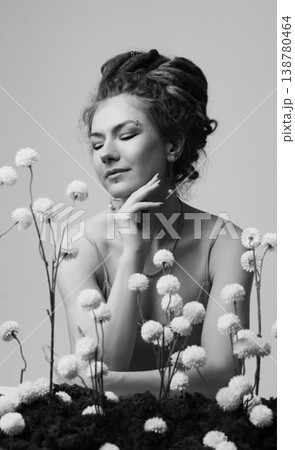 Young Caucasian redhead woman touching face among dried white flowers on moss, white wall Young Caucasian redhead woman touching face among dried white flowers on moss, white wall 138780464