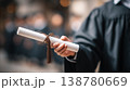 Graduation diploma in hand with academic robe ceremony background 138780669