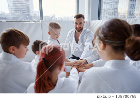Instructor guiding children during martial arts lesson with cheerful faces and focused expressions Instructor guiding children during martial arts lesson with cheerful faces and focused expressions 138780769