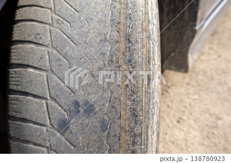 A close view of a worn car wheel reveals the metal cord. The setting appears to be a roadside, with dirt visible A close view of a worn car wheel reveals the metal cord. The setting appears to be a roadside, with dirt visible 138780923