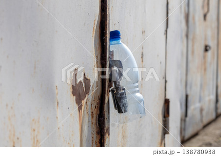 A garage door is closed and a plastic water bottle is used to secure the locking mechanism. The scene shows a typical afternoon A garage door is closed and a plastic water bottle is used to secure the locking mechanism. The scene shows a typical afternoon 138780938