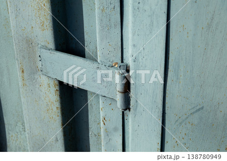Focus on the hinge of a metal garage door with a blue finish showing wear and tear in a suburban setting during daylight hours Focus on the hinge of a metal garage door with a blue finish showing wear and tear in a suburban setting during daylight hours 138780949