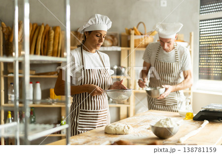 Elderly man and woman sift flour and whipping dough 138781159