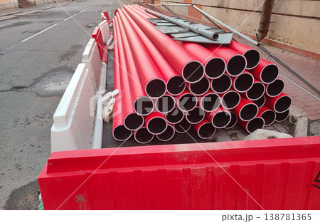 Bright red pipes stacked near a construction site on a city street in the daytime Bright red pipes stacked near a construction site on a city street in the daytime 138781365