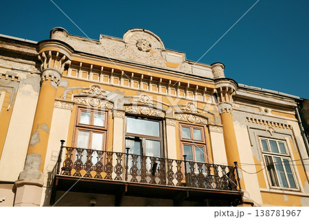 Historic yellow building facade with ornate decorations and balcony under clear blue sky in Sombor, Serbia. Classic European architecture and urban heritage concept 138781967