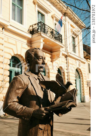 Bronze statue of Veljko Petrovic holding book with pigeon in front of historic building in Sombor, Serbia, cultural and artistic landmark 138781972