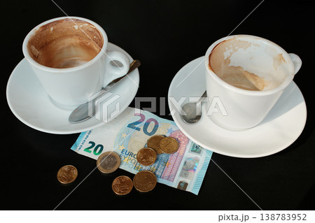 Two partially drunk cappuccino cups with euro banknote and coins on table. Concept of cafe payment for two people, coffee meeting and social spending Two partially drunk cappuccino cups with euro banknote and coins on table. Concept of cafe payment for two people, coffee meeting and social spending 138783952