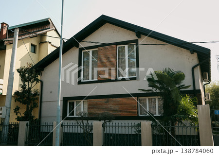 Modern residential house with wooden facade elements and palm tree in front yard. Suburban family home with contemporary architecture, private fence, and quiet neighborhood living concept 138784060