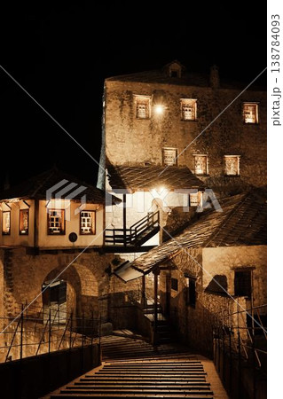 Night view of historic stone buildings in Mostar illuminated by warm lights. Traditional Balkan architecture and quiet atmosphere emphasize the timeless character of the old town 138784093