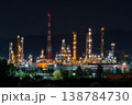 Workers operate machinery and equipment at an oil refinery during the night near hills and urban areas. Lights shine brightly 138784730