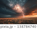 Dark clouds fill the sky as bright lightning lights up the horizon over the grassland at sunset. The scene shows nature's power 138784740