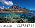 Fish swim in clear water near rocks below a mountain in Tahiti under a bright blue sky. The scene shows nature and water life 138784742