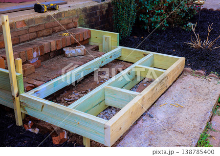 Construction of wooden frame for steps by brick wall in garden setting Construction of wooden frame for steps by brick wall in garden setting 138785400