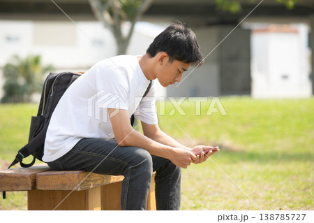 公園のベンチでスマートフォンを操作する男子学生 138785727
