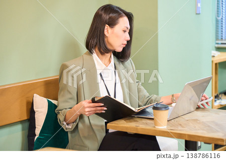 カフェ風のオフィスで手帳を確認しながらPC作業をするビジネスウーマン 138786116