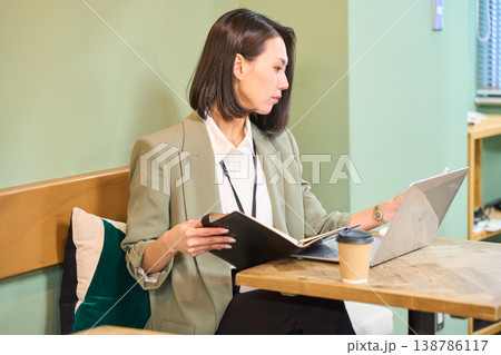 カフェ風のオフィスで手帳を確認しながらPC作業をするビジネスウーマン 138786117