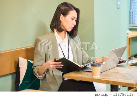 カフェ風のオフィスで手帳を確認しながらPC作業をするビジネスウーマン 138786118