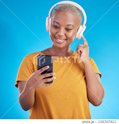 Woman, headphones and phone listening to music, audio streaming service and social media on a blue background. Young african person or influencer with electronics, techno or radio on mobile in studio 138787821