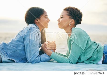 Love, ocean and sunset, lesbian couple on blanket together, holding hands on sand and holiday adventure. Lgbt women, bonding and relax on beach vacation with romance, pride and happy lying in nature. 138787871