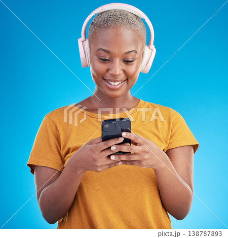 Woman, smartphone and headphones listening to music, audio streaming service or social media on blue background. Young african person or influencer chat on mobile for podcast subscription in studio Woman, smartphone and headphones listening to music, audio streaming service or social media on blue background. Young african person or influencer chat on mobile for podcast subscription in studio 138787893