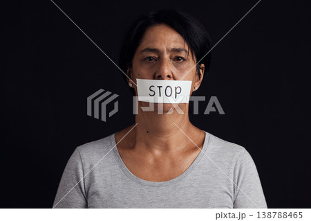 Portrait, stop and censorship with a woman in studio on a black background for gender equality or domestic violence. Face, silence or abuse and a scared female victim with her mouth covered in fear 138788465