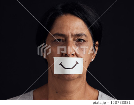 Portrait, fake smile or abuse and a mature woman in studio on a dark background with an expression. Depression, anxiety and mental health with a female person looking brave to hide her emotions Portrait, fake smile or abuse and a mature woman in studio on a dark background with an expression. Depression, anxiety and mental health with a female person looking brave to hide her emotions 138788881