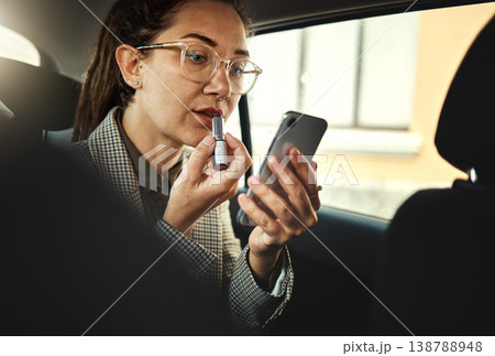 Phone, lipstick and a business woman in a car to travel in the city for work while multitasking. Face, mobile and makeup with a young female employee in a taxi or cab as a passenger for transport 138788948