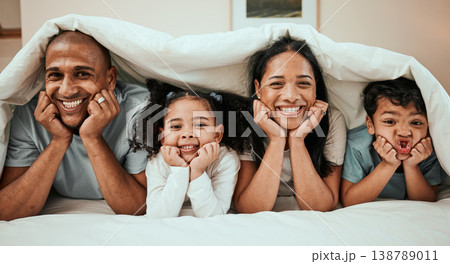 Happy, love and portrait of a family in bed with a blanket relaxing, resting and bonding at home. Happiness, smile and young children laying with their mother and father in the bedroom of their house 138789011