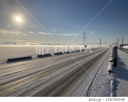 雪景色の平野を貫く一本道と冬の太陽 雪景色の平野を貫く一本道と冬の太陽 138789346