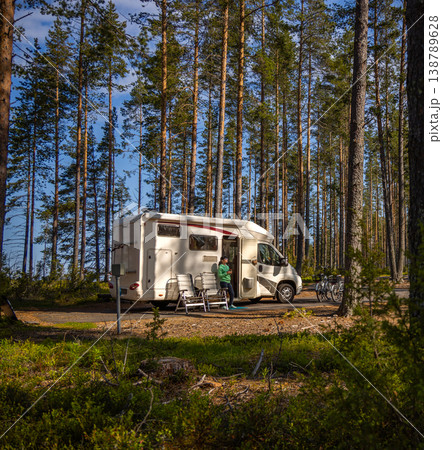 Woman with coffee standing near camper van in pine forest campsite. Woman with coffee standing near camper van in pine forest campsite. 138789628