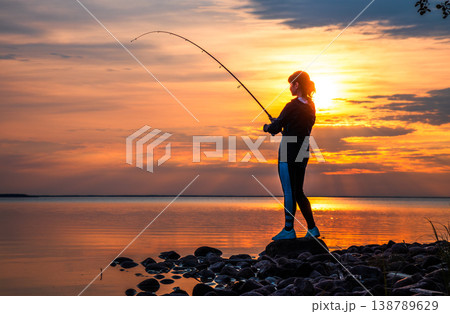 Silhouette of woman fishing on rocky lakeshore at sunset. Silhouette of woman fishing on rocky lakeshore at sunset. 138789629