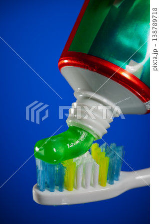 Green gel toothpaste being squeezed from tube onto colorful toothbrush bristles, dental hygiene and oral care concept on bright blue background. 138789718