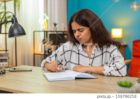 Indian woman writes in notebook crosses out lines then retries searching solution focused determined Indian woman writes in notebook crosses out lines then retries searching solution focused determined 138790258