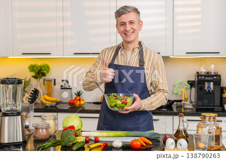 Middle-aged man showing fresh vegetable salad with thumbs up in kitchen for healthy eating routine Middle-aged man showing fresh vegetable salad with thumbs up in kitchen for healthy eating routine 138790263