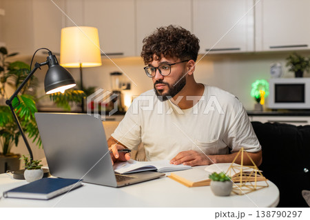 Arabian man studies online on laptop writes notes from video course prepares for exam at night 138790297