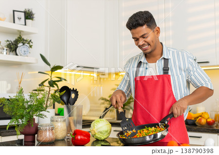 Indian man frying mixed vegetables in pan for healthy home meal prep and clean eating daily routine 138790398