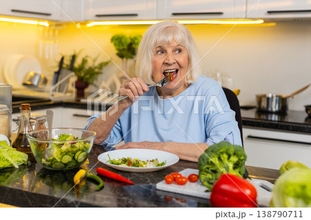 Senior old woman eating healthy salad in home kitchen thinking about diet plan choice and nutrition Senior old woman eating healthy salad in home kitchen thinking about diet plan choice and nutrition 138790711
