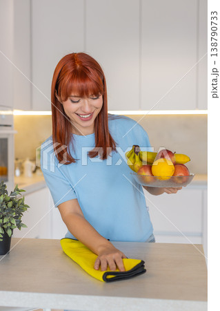 Young woman wipes kitchen countertop with microfiber cloth polishes surface shows clean tidy order Young woman wipes kitchen countertop with microfiber cloth polishes surface shows clean tidy order 138790733