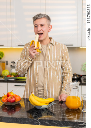 Middle-aged man eating banana in kitchen enjoying healthy eating for weight loss nutrition at home 138790838