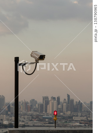 Perched above the sprawling, misty city, a lone security camera shares the rooftop with a crimson warning light, marking the skyline for passing aircraft. Perched above the sprawling, misty city, a lone security camera shares the rooftop with a crimson warning light, marking the skyline for passing aircraft. 138790965