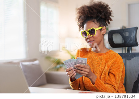 Young African American woman with surprised expression holding bunch of hundred dollar bills Young African American woman with surprised expression holding bunch of hundred dollar bills 138791334