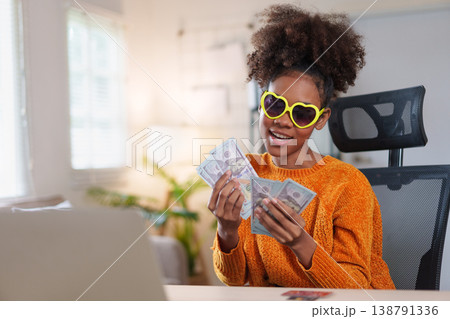 Young African American woman with surprised expression holding bunch of hundred dollar bills Young African American woman with surprised expression holding bunch of hundred dollar bills 138791336
