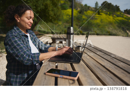 Woman working on laptop with smartphone on table outdoors Woman working on laptop with smartphone on table outdoors 138791818